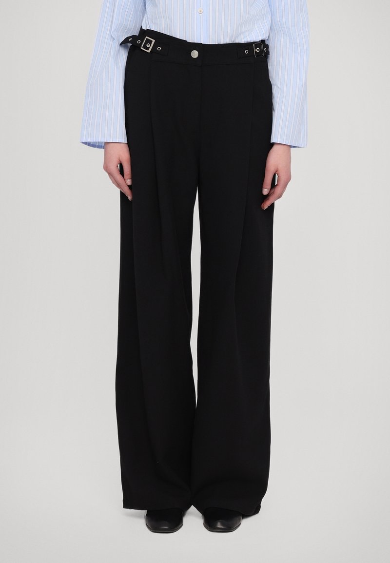 Zwarte wijde broek van soepel stof, voorzien van een tailleband met zilverkleurige gesp en een knoopsluiting.