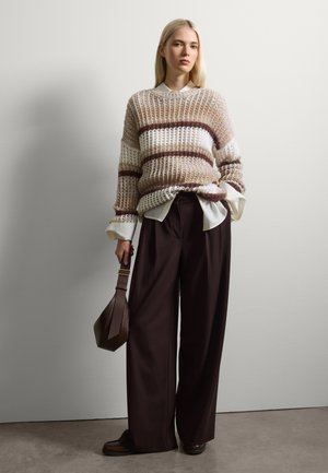 Suéter de punto con un corte holgado, con franjas marrones y crema. Combinado con pantalones oscuros amplios y un pequeño bolso marrón.
