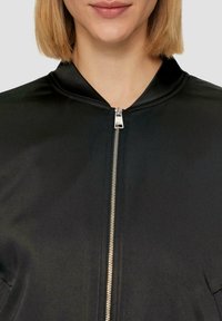 Zwarte bomberjack met een gladde, satijnen afwerking. Voorzien van een ritssluiting en een klassiek kraagontwerp. Minimalistische stijl zonder patronen of accenten.