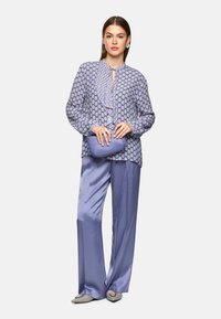 Hellbluse mit Muster und Rüsche am Hals, kombiniert mit hellblauen satinierten weit geschnittenen Hosen und einer passenden Clutch.