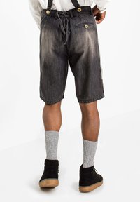 Pantaloni corti in denim scuro con un design sbiadito, dotati di vita con cordoncino, bretelle e tasche laterali. Abbinati a calzini grigi a coste e scarpe nere.