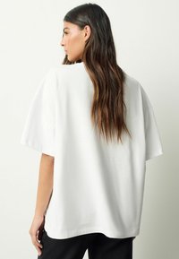 Weißes Baumwoll-T-Shirt mit kurzen, weiten Ärmeln und einem lockeren Schnitt. Es hat einen runden Halsausschnitt und eine glatte, weiche Textur.