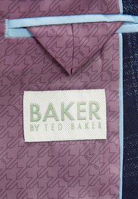 Paarse stof met geometrisch patroon, voorzien van een wit label met de tekst "BAKER" in het groen, verfraaid met lichtblauwe rand.