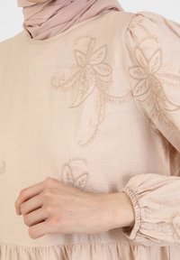 Světle růžový dlouhý rukáv oděv s květinovou výšivkou, kulatým výstřihem a nařasenými rukávy. Měkká textura a splývavý design.