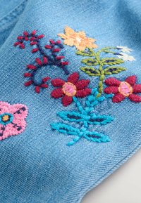 Denim szövet színes virágmintával, rózsaszín, piros, narancs és kék virágokkal, világoskék háttérrel kontrasztban.