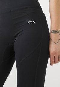 Leggings neri aderenti, con una finitura texturizzata e il logo "ICIW" in evidenza. I dettagli delle cuciture aggiungono definizione al design.