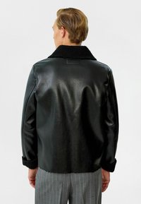 Zwarte leren jas met een fluffy zwarte kraag en manchetten, met een strakke textuur en eenvoudig ontwerp. Gekleed met grijze panterstripes.