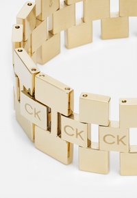 Pulsera de oro con eslabones rectangulares de acabado pulido, grabada con "CK" en algunos eslabones, que muestra un diseño moderno y una textura suave.