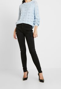 Pullover lavorato a maglia di un blu chiaro con un motivo a diamante, abbinato a pantaloni cargo neri slim fit e tacchi alti neri.