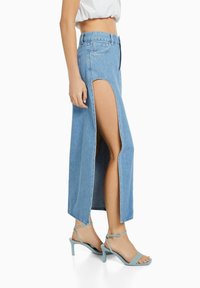 Ljusblå jeanskjol med höga sidslitsar, utrustad med en åtsittande midjeband och rak silhuett. Kombinerad med ljusblå klacksandaler.