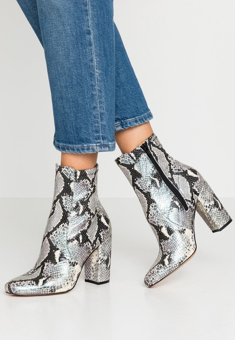 Botines hasta el tobillo con estampado de piel de serpiente, acabado brillante, detalles en negro y cremallera lateral. El tacón es grueso y mide aproximadamente 9 cm.