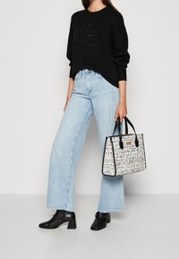 Suéter negro con un logo, jeans de pierna ancha de color azul claro y un bolso blanco con un patrón abstracto en negro, combinado con botas negras de tobillo.