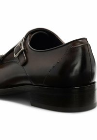 Scarpa di pelle marrone con design elegante, presenta un accento in fibbia argentata, finitura testurizzata e un tacco impilato nero resistente.