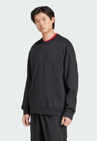 Sort sweatshirt i bomuldsblanding, rund hals, ribbede manchetter, diskret logo på brystet, parret med løse sorte bukser. Blød tekstur, afslappet pasform.