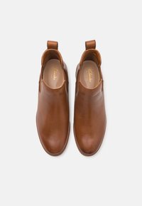 Botines de cuero marrón con un acabado suave, punta redonda, paneles laterales elásticos y tiradores para facilitar su uso. Suelas planas.