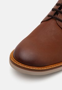 Chaussure en cuir marron avec une finition lisse, bout arrondi et une semelle en caoutchouc cousue avec une accent orange le long du bord.
