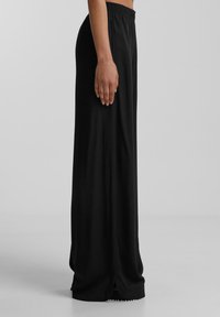 Pantaloni neri a gamba larga con cintura elasticizzata, realizzati in tessuto morbido, con una leggera lucentezza e dettagli a scallop all'orlo delle caviglie.