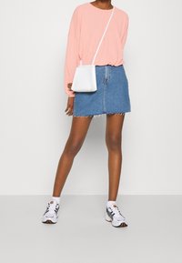 Vaaleanpunainen pitkähihainen paita yhdistettynä siniseen farkku-minihelmaan. Valkoinen olkalaukku, jossa on teksturoitu pinta. Valkoiset ja mustat urheilukengät.