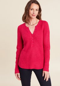 Helles pinkes Rippensweatshirt mit einem V-Ausschnitt, dekorativen Kn�öpfen und strukturiertem Muster. Lange Ärmel verjüngen sich an den Handgelenken. Kombiniert mit dunklen Hosen.
