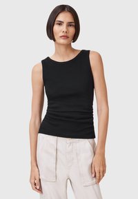 Top senza maniche nero con scollo rotondo e dettaglio arricciato ai lati, realizzato in un morbido tessuto elasticizzato. Abbinato a pantaloni chiari.