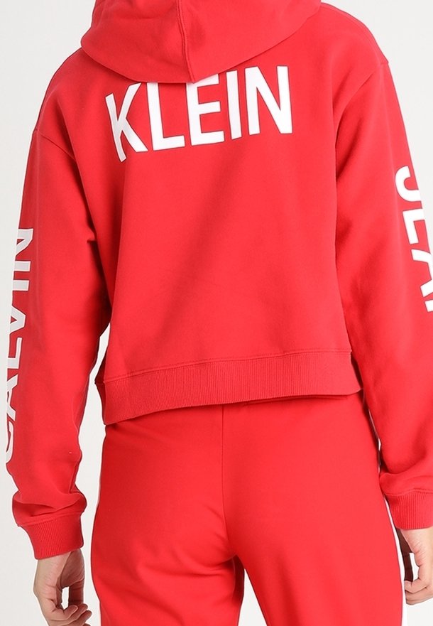 Felpa rossa corta con cappuccio, con grande logo bianco "KLEIN" sul retro e la scritta "JEANS" lungo la manica sinistra, realizzata in tessuto morbido.