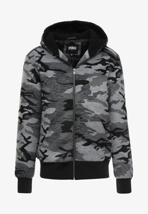 Hallituseta mantli pehme tekstuuriga halli kamuflaažimustriga kapuutsiga vetsag. Kanga sees on must fliisvooder ja soonikkoes varrukad.