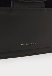 Juodas odinis rankinukas, pasižymintis lygiu paviršiumi, minimalistiniu dizainu ir auksiniu "KARL LAGERFELD" logotipu priekyje.