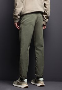 Olivově zelené kalhoty s uvolněným střihem, vyrobené z měkkého materiálu, mají boční kapsy a jsou upravené s ohrnutými nohavicemi. V kombinaci se šedými teniskami.