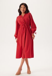 Abito midi rosso con maniche lunghe, chiusura a bottoni frontale, vita elastica e dettagli con coulisse. Tessuto morbido con una vestibilità morbida e orlo a lunghezza ginocchio.