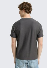Tricou scurt cu mânecă scurtă de culoare gri închis, cu decolteu rotund, având o textură subtilă și o croială relaxată, expus pe un fundal deschis.