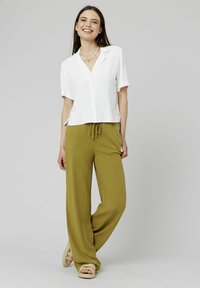 Chemise blanche à manches courtes avec boutons, associée à un pantalon ample vert olive à taille élastique. Le modèle porte des sandales en plateforme tressées.