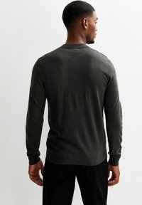 Dunkelgrüner Strickpullover mit langen Ärmeln, gerippten Bündchen und Saum, von hinten präsentiert. Geschmeidige Textur und taillierter Schnitt.