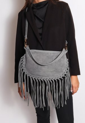 Grijze suède schoudertas met franjes, ronde vorm, decoratieve stiksel en een verstelbare schouderband. Hardware in goudkleur.