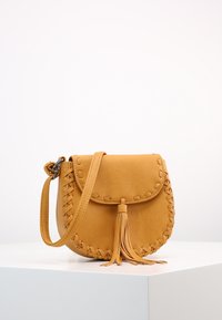 Borsa a tracolla in pelle gialla di forma rotonda, con dettagli intrecciati e una nappina sul davanti. Texture liscia con chiusura a pattina.