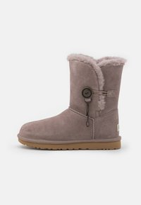 Bota de invierno de ante malva de altura media con forro interior esponjoso, botón de anclaje y cierre de lazo, y suela de goma marrón clara.
