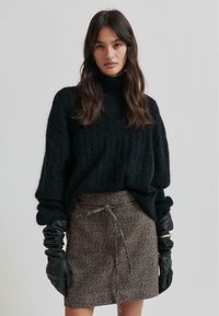 Svart stickad tröja med v-ringning och ribbad struktur, tillsammans med en brun tweed mini kjol med dragsko, och svarta skinnhandskar.