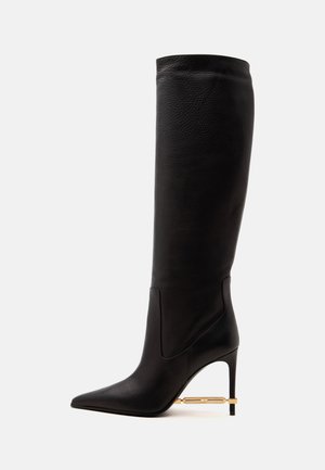 Botte haute en cuir noir à bout pointu avec un talon aiguilles fin et un détail décoratif en métal doré près du talon.