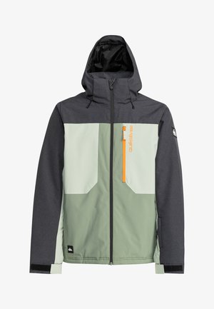 Chaqueta impermeable gris y verde claro con capucha, cremallera naranja, bolsillo en el pecho y texturas de tela contrastantes. Presenta el logo en la manga.