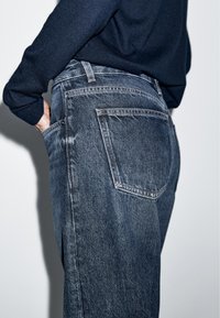 Denim jeans in dark blue with a faded finish, featuring a high waist, back pockets, and subtle stitching details.