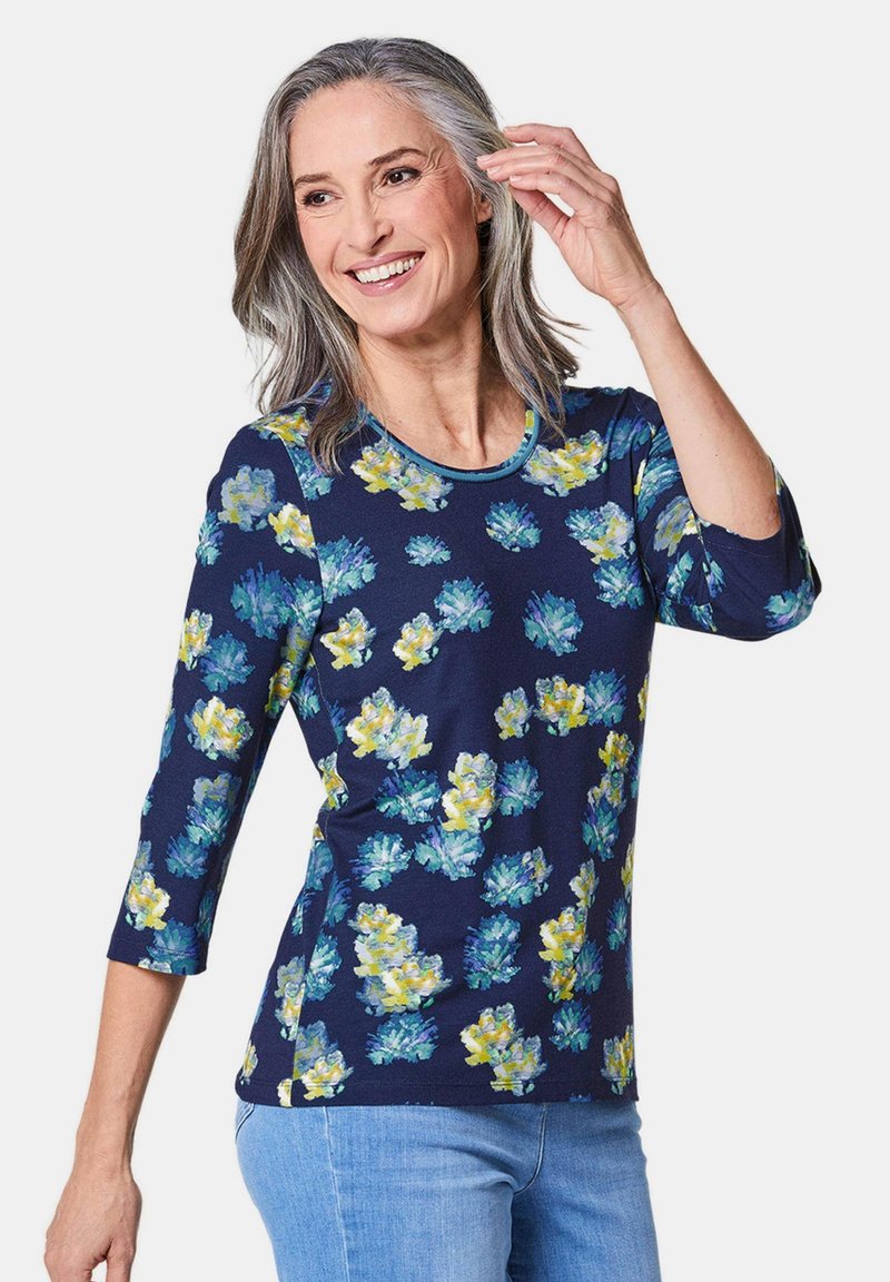 Marineblaues T-Shirt mit floralem Muster in Blau, Gelb und Grün. Verfügt über einen runden Ausschnitt und Dreiviertelärmel, aus weichem Stoff gefertigt.