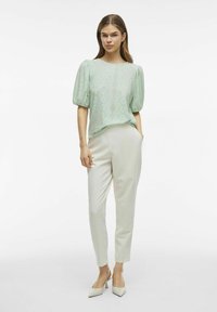 Top verde menta a maniche corte con maniche a palloncino, caratterizzato da un delicato motivo a occhielli. Abbinato a pantaloni crema e scarpe con punta beige.