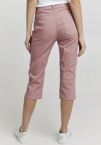 Jeans cortos rosas con una textura suave, dos bolsillos traseros y una etiqueta en la cintura. Combinados con zapatillas blancas.