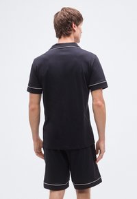 Μαύρο πόλο μπλουζάκι με λευκή επένδυση, όψη από πίσω, σετ με μαύρο σορτς που ταιριάζει. Απλός σχεδιασμός, κοντά μανίκια και κλασικός γιακάς.