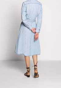 Ljusblå denimklänning med långa ärmar, midjeband och utsvängd nederkant. Har knäppte manschetter och en mjuk, något texturerad yta.