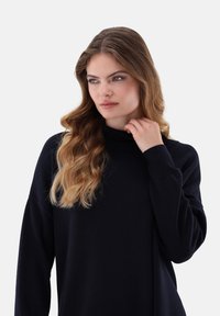 Dunkelblauer Rollkragenpullover mit langen Ärmeln, aus einem weichen Material gefertigt, mit einer lockeren Passform und dezentem Rippenstrickmuster.