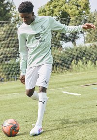 Világoszöld, hosszú ujjú focimez magas gallérral, fehér rövidnadrággal, fehér zoknival, és színes futballcipőkkel, narancssárga és fekete labdával párosítva.