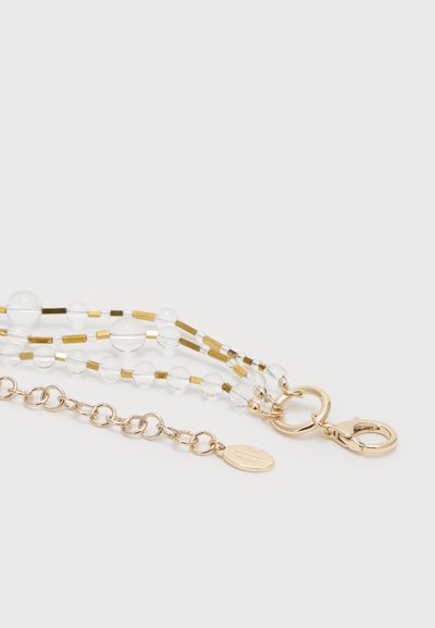 Guldspænde og kæde med klare runde perler og små gyldne rektangulære perler på et flerstrenget armbånd eller halskæde, på hvid baggrund.