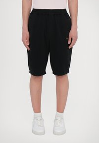 Black shorts made of cotton with an elastic waistband. Features a small gold logo on the front. Paired with white sneakers and socks.
