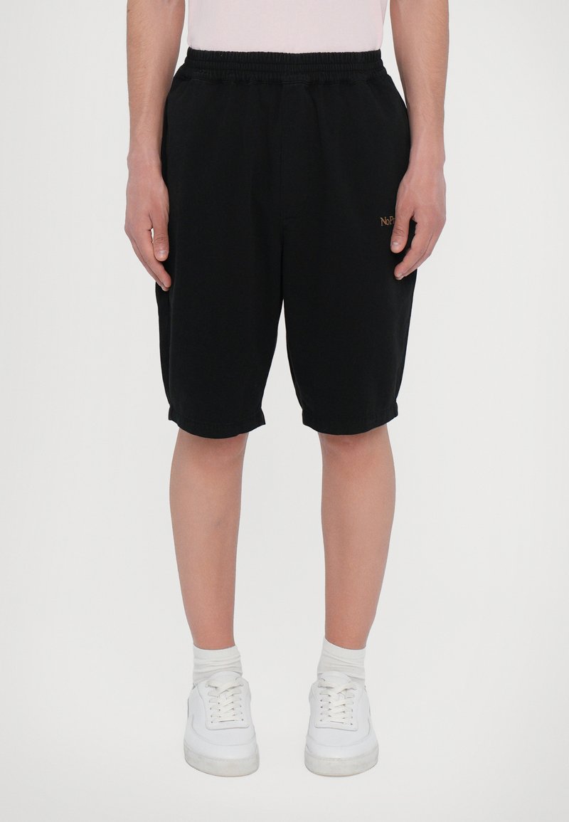 Black shorts made of cotton with an elastic waistband. Features a small gold logo on the front. Paired with white sneakers and socks.