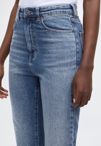 Modre kavbojke iz jeansa z visokim pasom in oprijetim krojem, z zapiranjem na gumbe, sprednjimi žepi in nežnimi šivi na šivih.